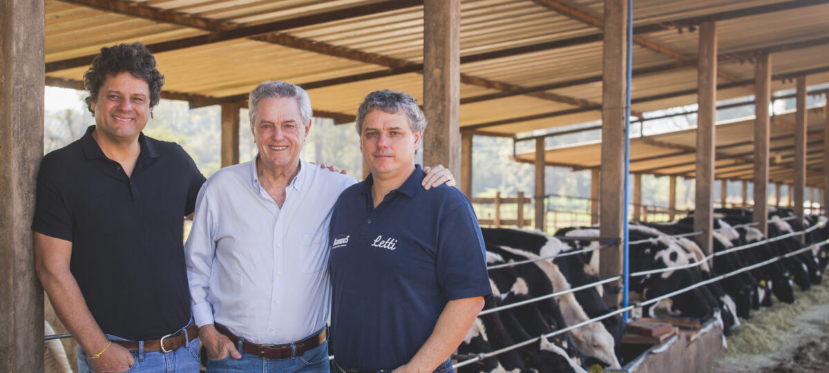 Three men in a dairy barn pose for the camera