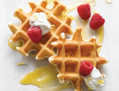 Waffles with cream and raspberries arranged on a white plate