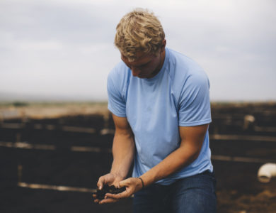 A man in a blue shirt holds a handful of rich soil