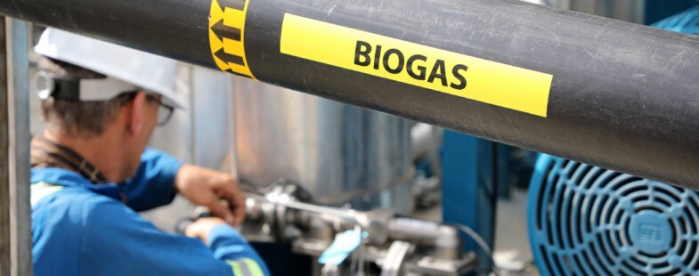 A man in a safety helmet and blue overalls working on an industrial biogas project