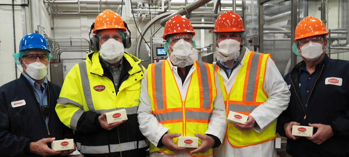 A group of men in safety gear pose for the camera at a dairy processing plant