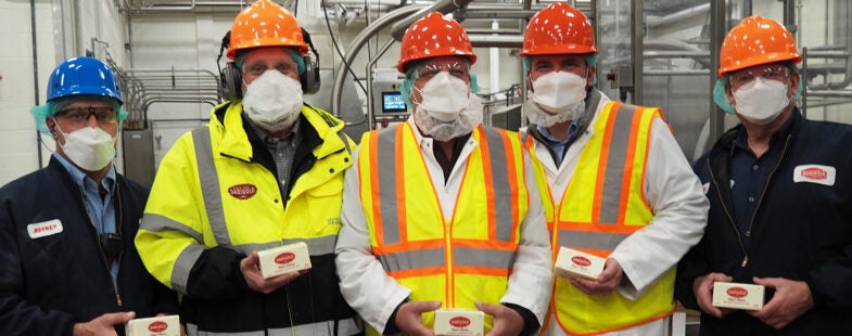 A group of men in safety gear pose for the camera at a dairy processing plant