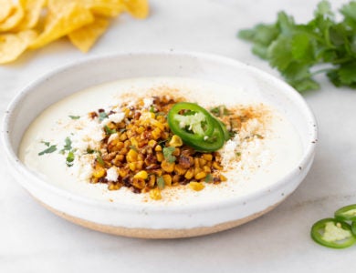 A white bowl of dip topped with corn and jalapeños