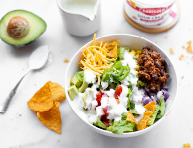 A bowl of taco salad, with chips, an avocado and sour cream