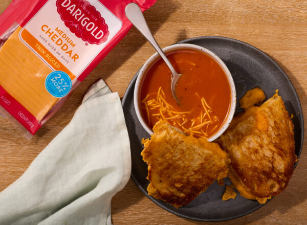 Creative product shot featuring Darigold thin sliced medium cheddar with a grilled cheese sandwich and tomato soup
