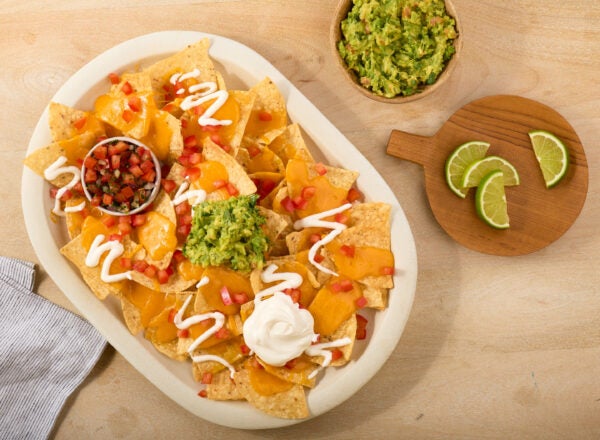 Stock photo of nachos with guacamole, sour cream, lime, salsa and melted cheese