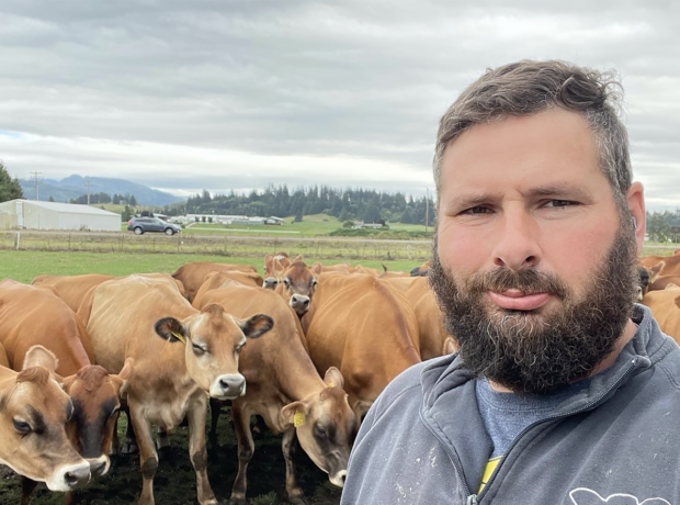 A man poses for the camera with a small group of brown cows behind him