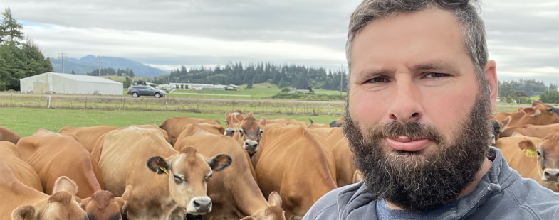 A man poses for the camera with a small group of brown cows behind him