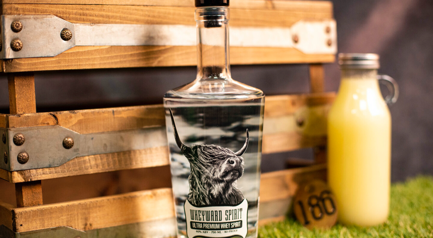 A clear bottle of liquor next to a bottle of whey in front of a wooden crate