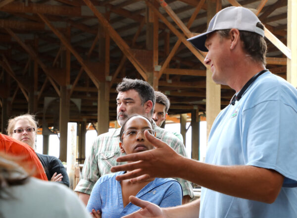 A tall man in a cap talks to a group of people outside