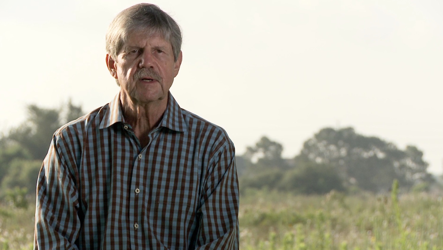 A man poses for the camera outside in a rural area