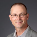 A man with a grey jacket and glasses poses for the camera