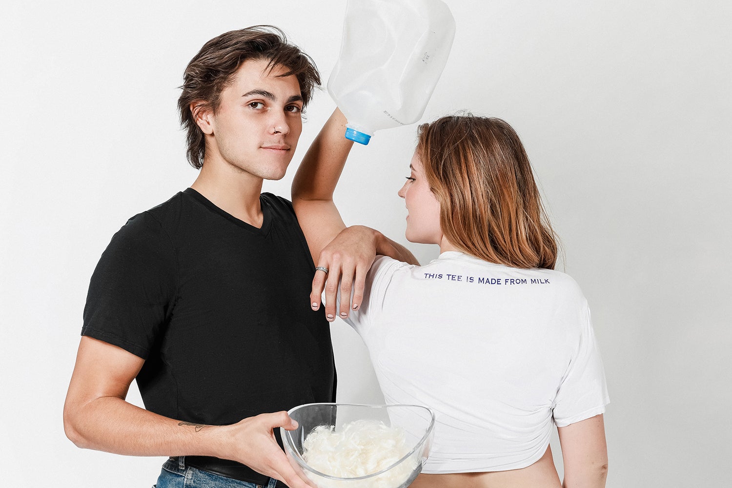 A man and woman pose with a milk jug and a bowl of white milk fiber