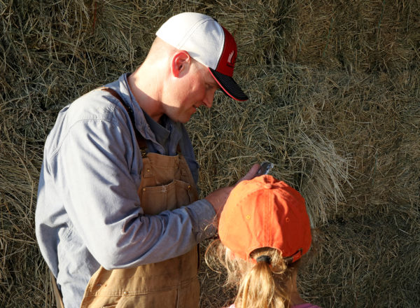 Man looking at a phone with a girl in front of hay bales