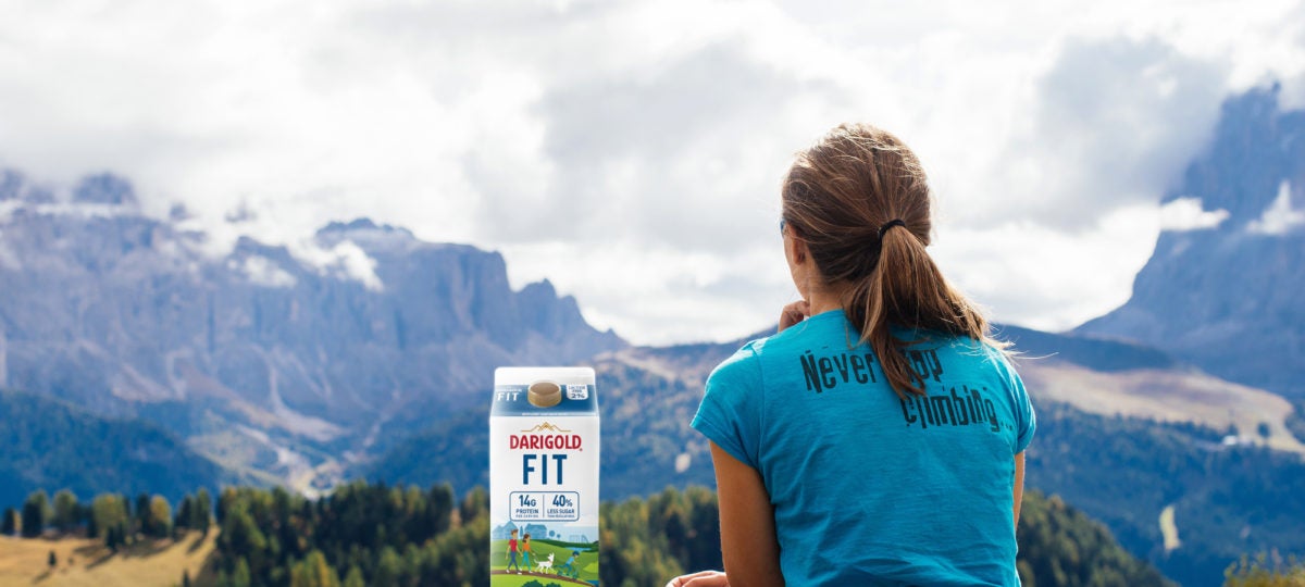 Girl in blue shirt looks at a mountain view with a carton of milk next to her