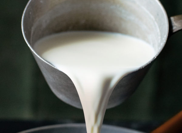 Milk in an old school metal pot being poured into another pot