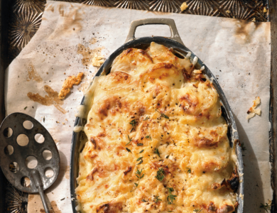 A pan full of cooked au gratin potatoes and a spoon with holes in it