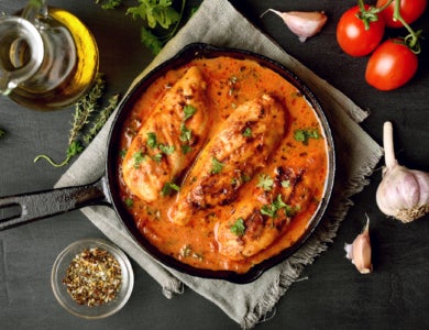 A cast iron pot with three chicken breasts in orange sauce