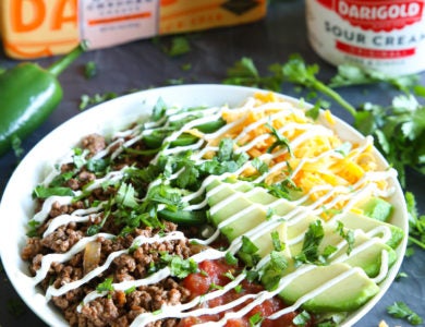 A taco salad with a white dish surrounded by peppers, sour cream and a block of cheese