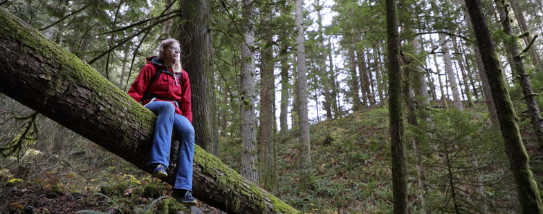 Woman in red jacket sitting on a log in the forest