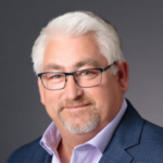 A man with white hair and square-rimmed glasses poses for the camera