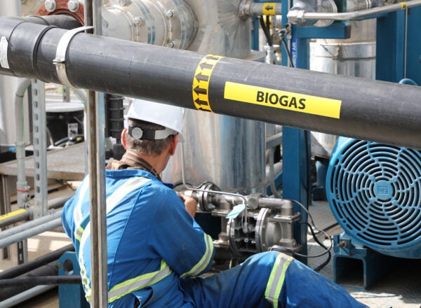 Man wearing blue uniform working on biogas equipment