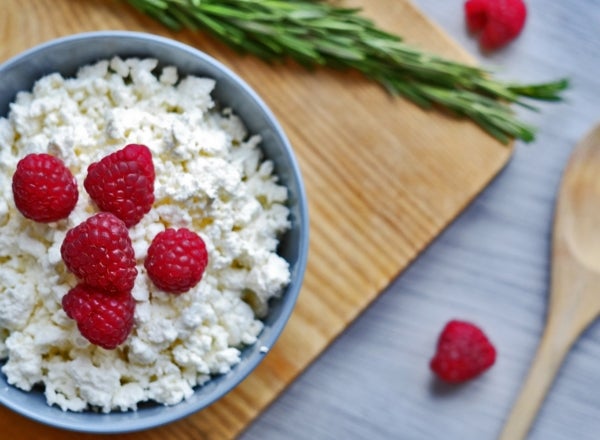 Creative food art shot featuring cottage cheese and raspberries — with rosemary and a wooden spoon and cutting board for decoration
