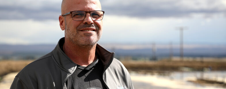 Man wearing glasses poses for the camera in front of agricultural land