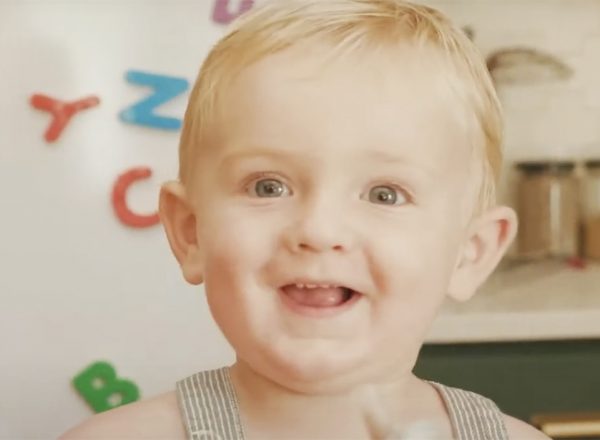 A little blonde kid smiles in the kitchen