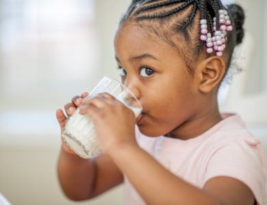 Header image of a cute little girl sitting in the kitchen drinking a glass full of milk.