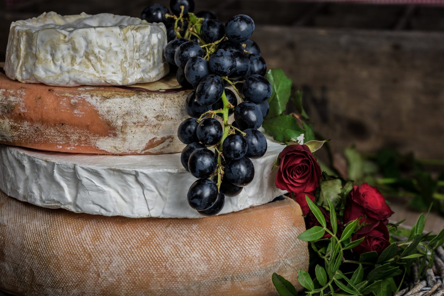 A stack of cheese with black grapes and a rose