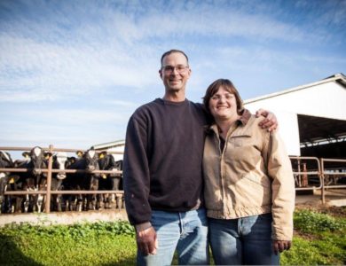 A couple pose for the camera with cows behind them