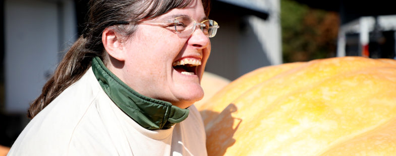 A woman laughing in front of a giant pumpkin