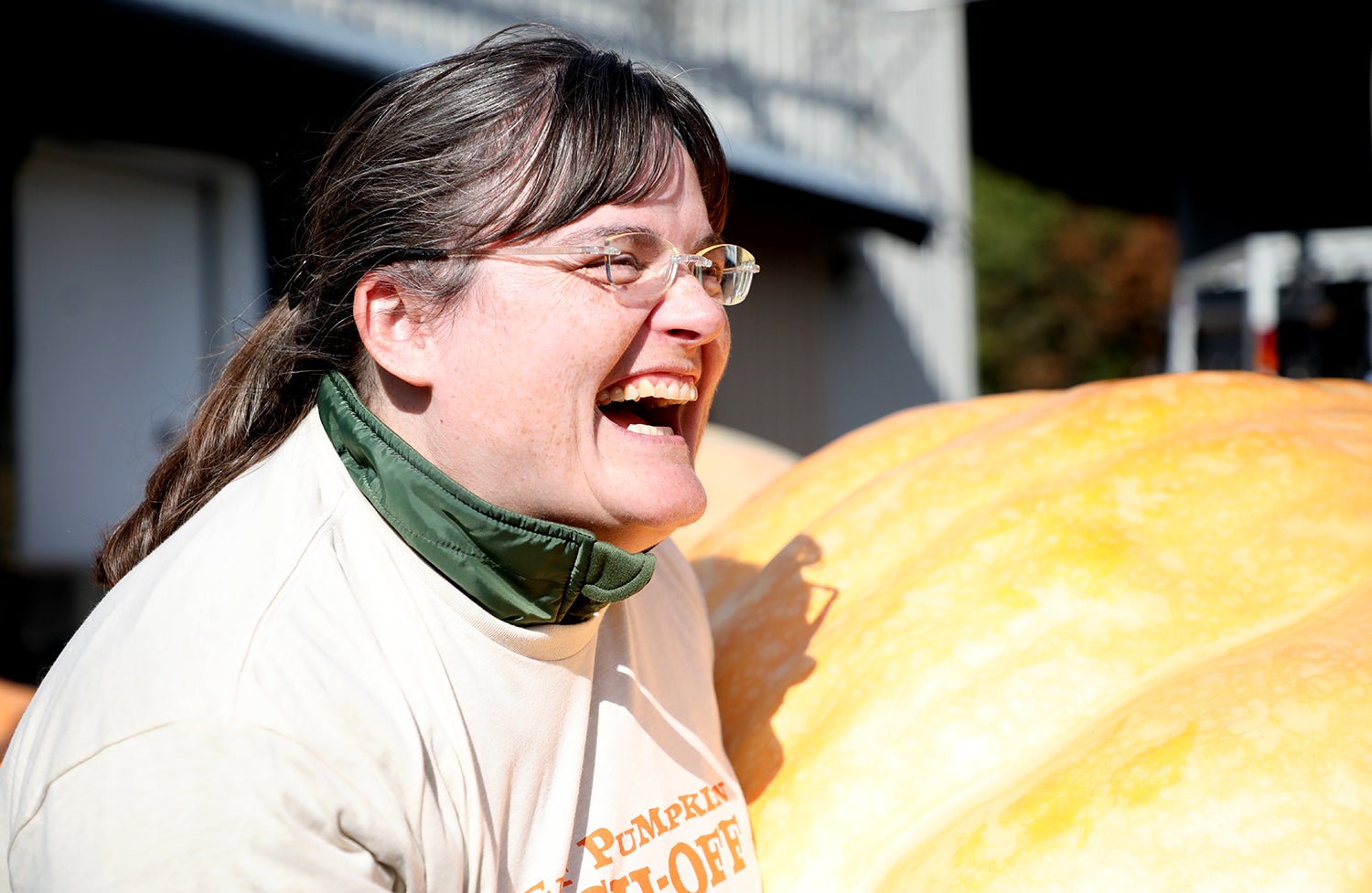A woman laughing in front of a giant pumpkin
